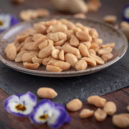 Erdnüsse geröstet ungesalzen dargestellt in Schale auf Schieferplatte mit Dekoration