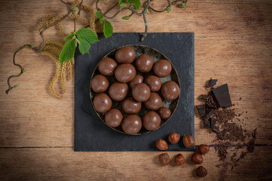 Vollmilchschokolade überzogene Haselnüsse in Schale auf Schieferplatte dekoriert mit Schokoraspel und Haselnüssen