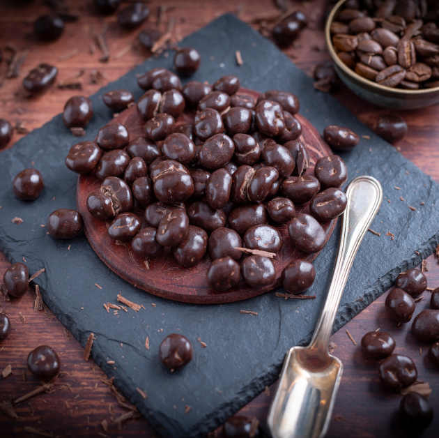 Kaffeebohnen umhüllt mit Schokolade auf Schieferplatte platziert auf Holztisch. Dekoriert drumherum mit Kaffeebohnen