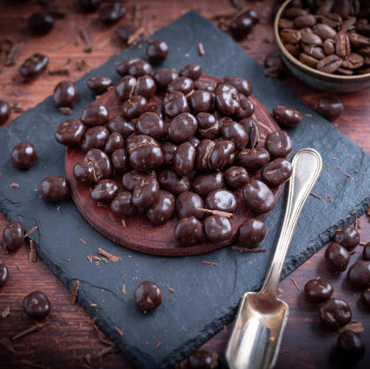 Kaffeebohnen umhüllt mit Schokolade auf Schieferplatte platziert auf Holztisch. Dekoriert drumherum mit Kaffeebohnen