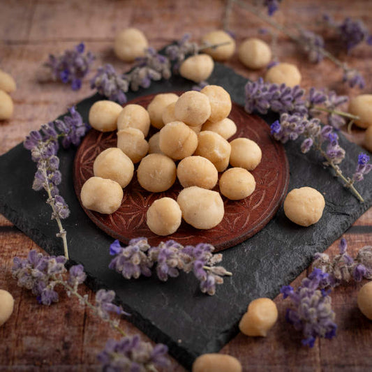 Macadamiakerne aus Kenia Style 1 mit sehr wenigen halben Kernen. Ansicht in Schale auf Schieferplatte und Holztisch mit Blumendekoration