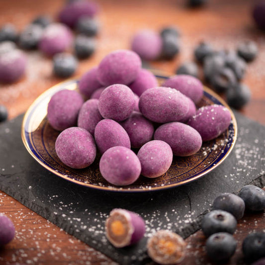 Seitenansicht nussmart schokolierte Blaubeermandeln auf Schieferplatte dekoriert mit Blaubeeren drumherum