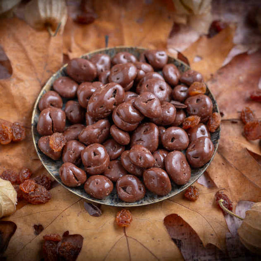 Schoko Rosinen Vollmilch von nussmart. Zart schmelzend lecker nach Schokolade harmonierend mit den Rosinen. Szenenbild exemplarisch Inhalt auf Teller und mit Blätter dekoriert.