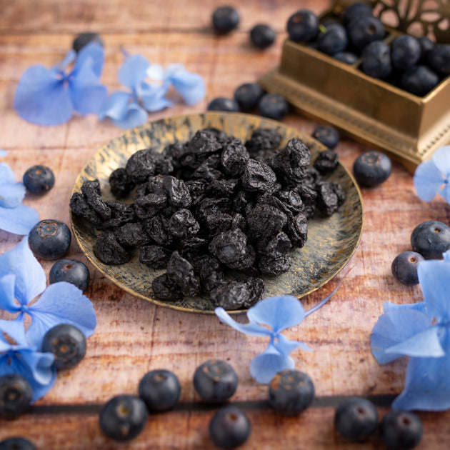 Getrocknete Blaubeeren von nussmart. Seitenansicht mit Szene. Blaue Blumenblüten um die Beeren