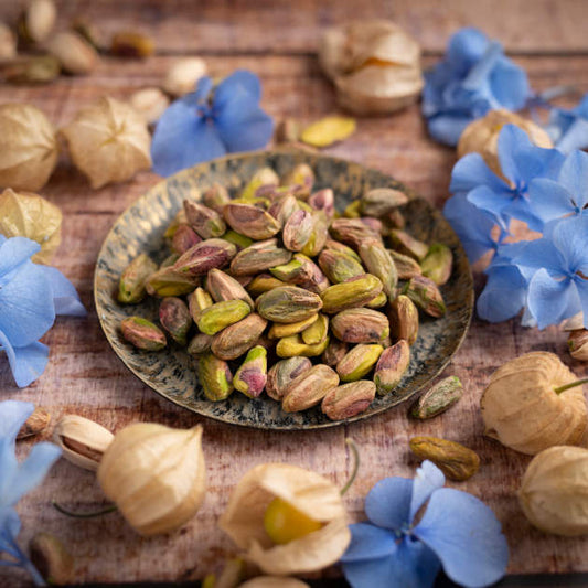 Ansicht Pistazienkerne aus den USA dekoriert in Schale auf Holztisch und blauen Blumenblüten drumherum