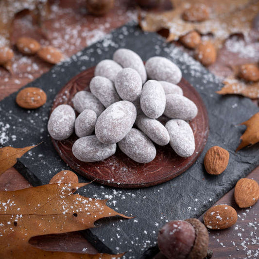 Schneemandeln oder nussmart schokolierte Vollmilchmandeln mit Puderzucker bestäubt. Ansicht auf Schieferplatte und Holztisch
