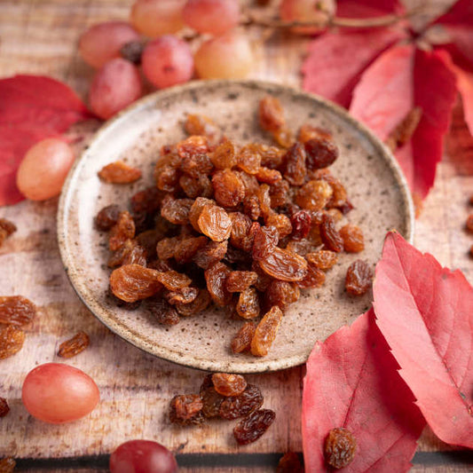 Ausgesuchte Sultaninen von nussmart Größe 10 . Ansicht in Schale mit herbstlichen Blättern drumherum dekoriert auf Holztisch