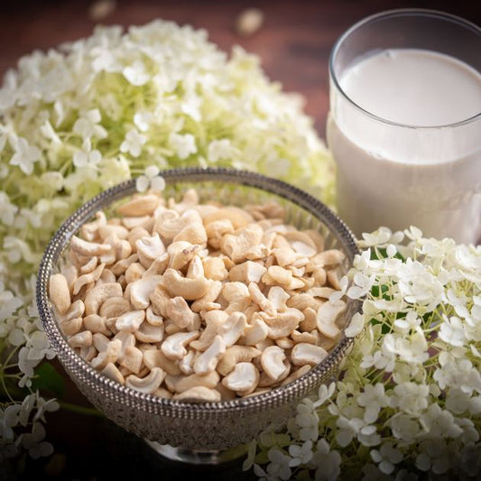 Cashewbruch. Ideal um Cashewmilch mit deinem Mixer zu zaubern. Seitenansicht der Cashew Stücke Large White Pieces (LWP) mit Deko drumherum und Glas Cashewmilch. Deko und Milch gehören nicht zum angebotenen Artikel