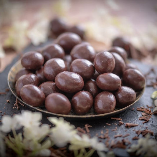 Schoko Macadamia in Zartbitterschokolade umhüllt. Ansicht von Seite. Platziert in Schale und Schieferplatte. it Deko drumherum