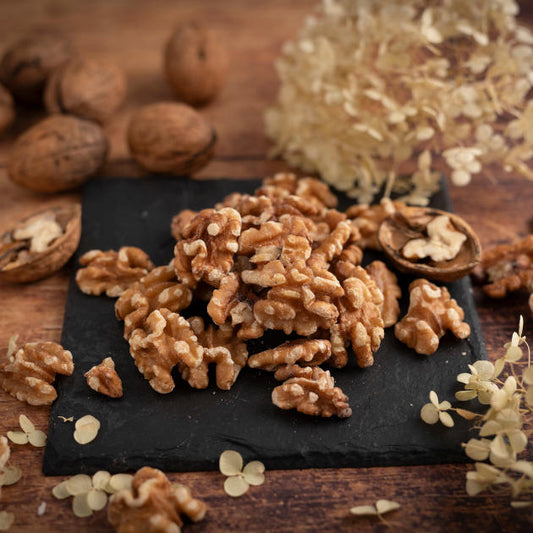 Walnusskerne aus den USA. Ausgesuchte Premiumqualität der Sorte Chandler. Ansicht auf Schieferplatte mit Deko drumherum auf Holztisch