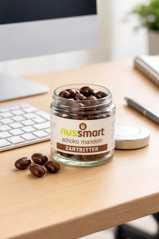 Zartbitter Schoko Cashews im Glas auf Schreibtisch mit Kaffee und Tastatur